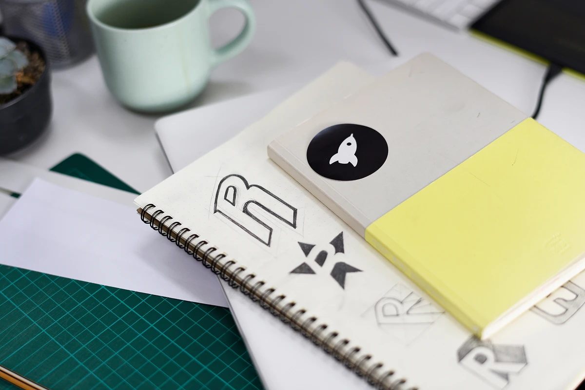 Sketchbook with hand-drawn logo concepts and notebooks on a designer’s desk.