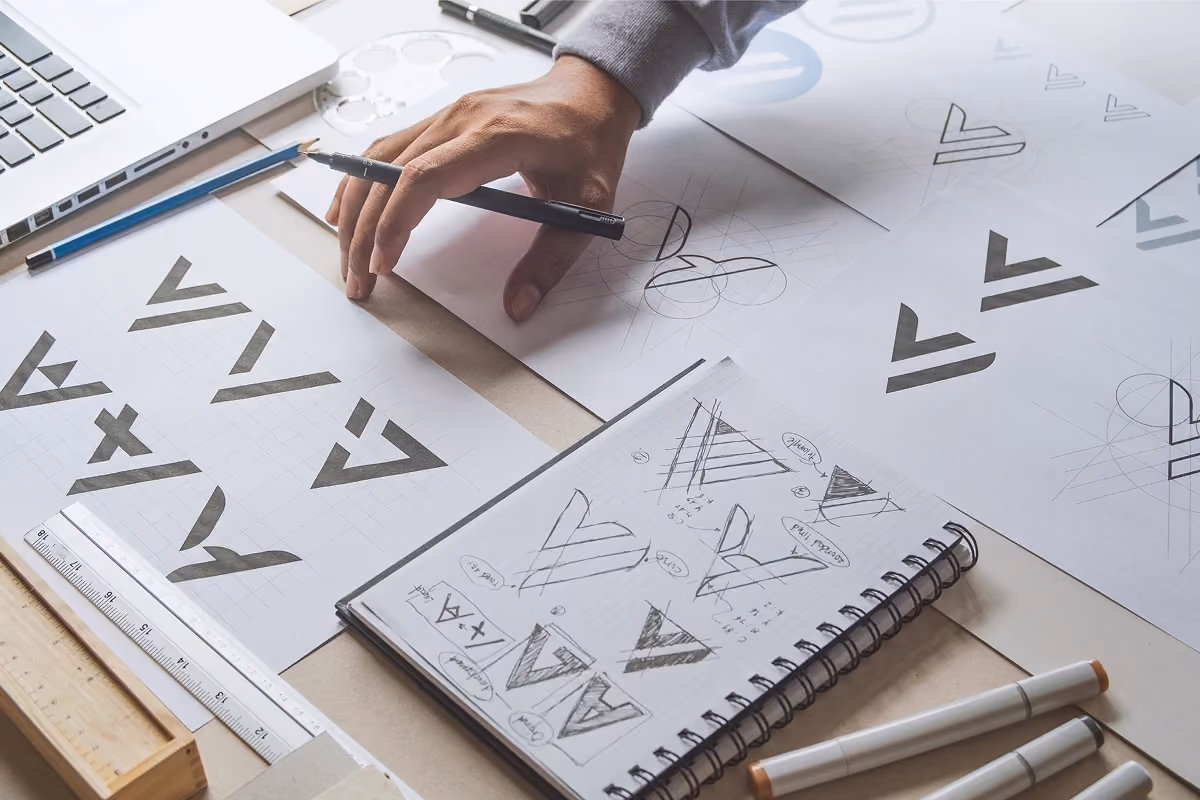Designer sketching and refining logo ideas on paper, surrounded by design tools and sketches.