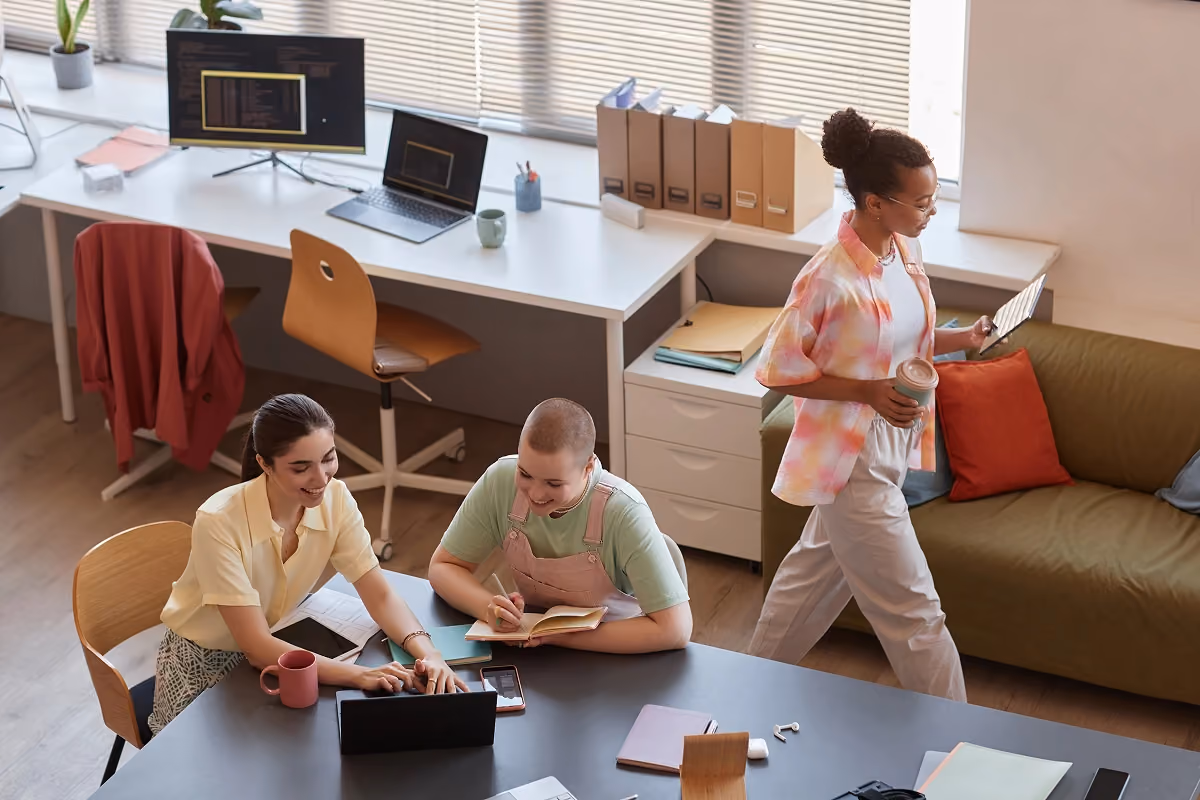 Three young professionals collaborating in a creative office space, working on laptops and tablets.