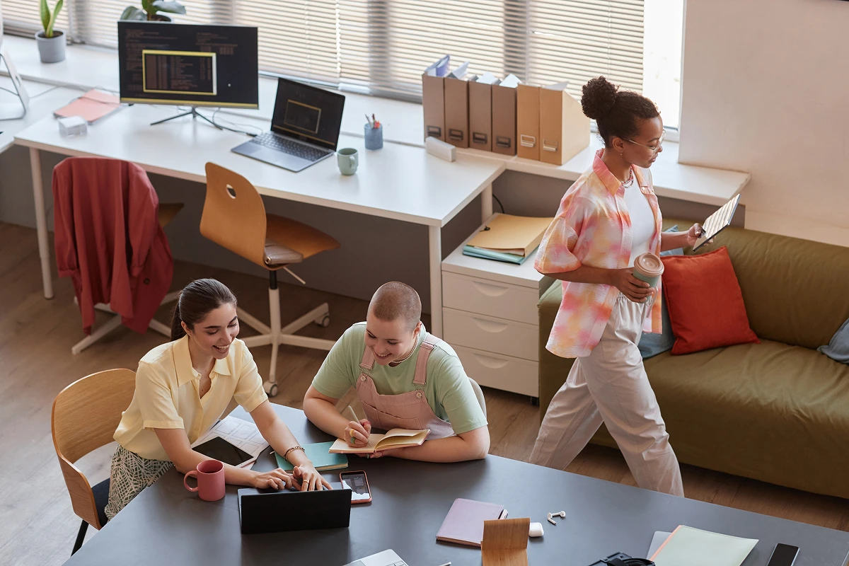 Three young professionals collaborating in a creative office space, working on laptops and tablets.