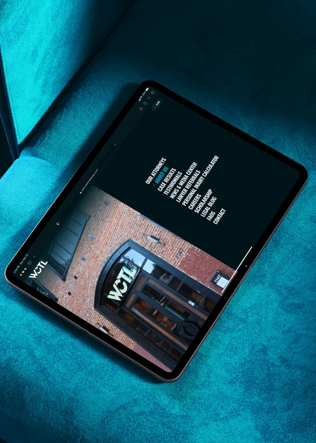 Tablet on a turquoise surface showing the WCTL website with a view of a brick building entrance and navigation menu.