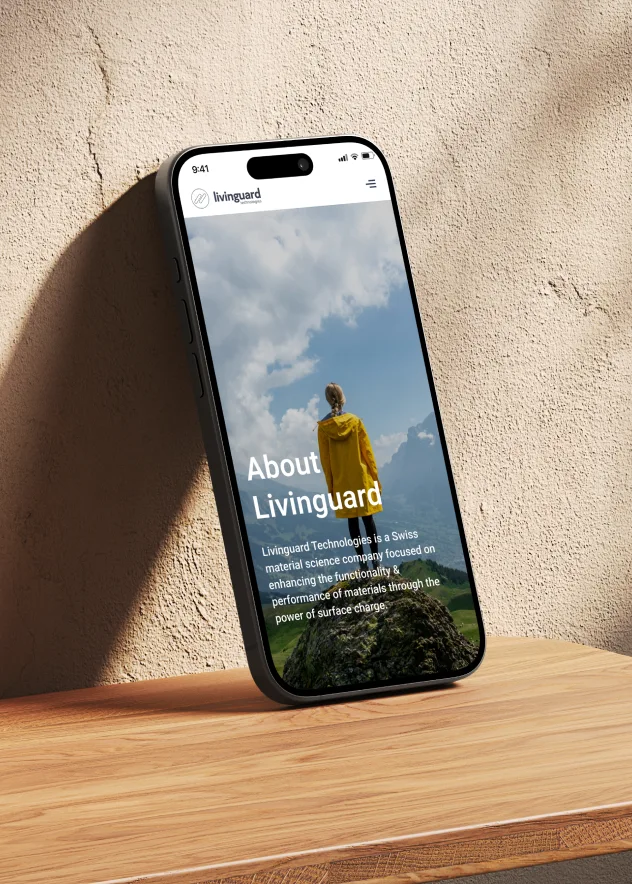 Smartphone displaying Livinguard website with a woman in a yellow jacket standing on a mountain top, symbolizing innovation in material science.