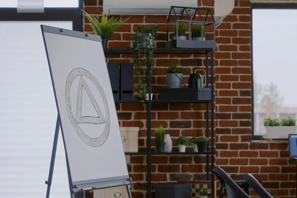 Sketch of a triangular logo on a flip chart in a loft-style office with brick walls and indoor plants.