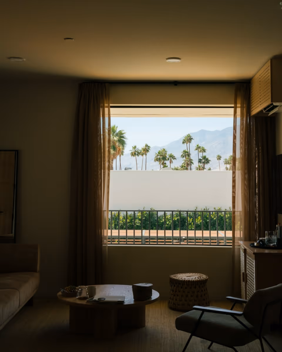  Interior of a modern room with a large window view of palm trees and distant mountains.