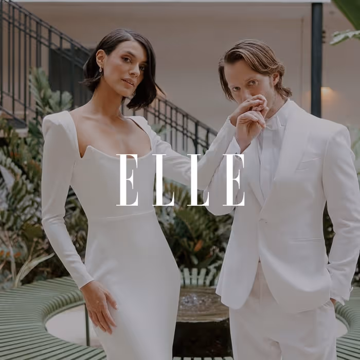 Fashion-forward bride and groom dressed in white, posing elegantly in a modern indoor venue, featured in ELLE.