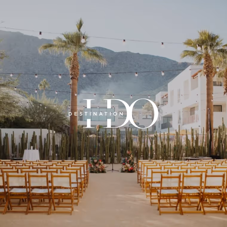Outdoor wedding ceremony setup with bamboo chairs, palm trees, string lights, and mountain views, featured in Destination I Do.