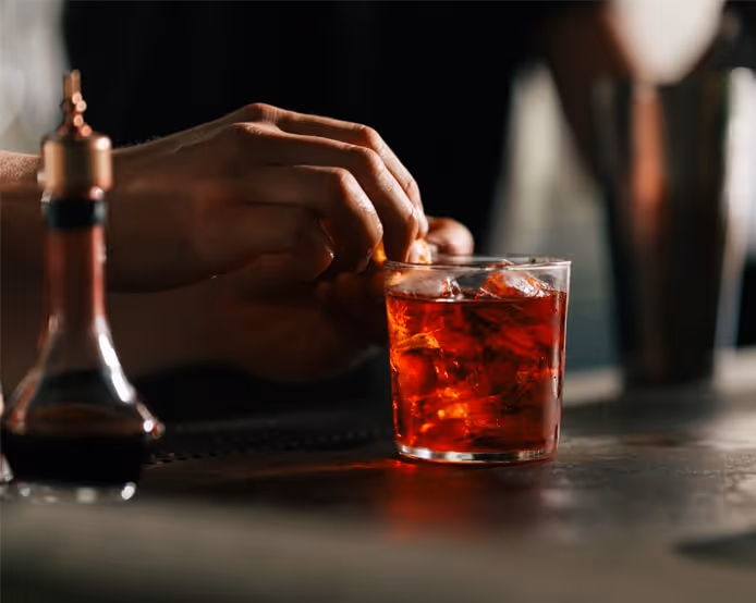 Bartender preparing a classic Negroni cocktail with orange garnish and ice in a glass