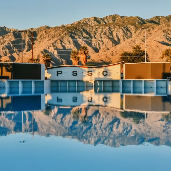 Palm Springs Swim Club pool reflecting desert mountains and palm trees under clear morning light.