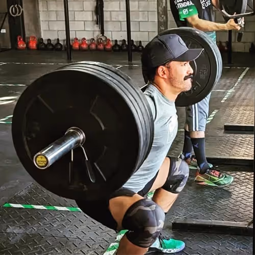 Man performing a heavy barbell squat during a strength training session at a CrossFit gym.