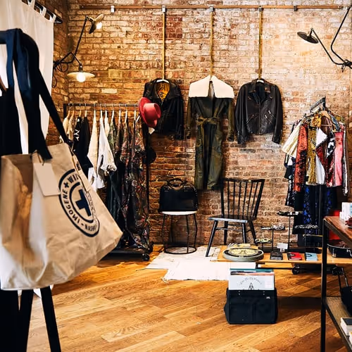 Stylish boutique with brick walls, hanging leather jackets, and racks of vintage outfits arranged around wooden flooring and modern industrial lights.