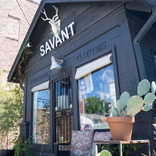 Exterior of Savant Vintage shop with dark wooden facade, antler decor, cactus plants, and signage advertising furnishings and vintage clothes.