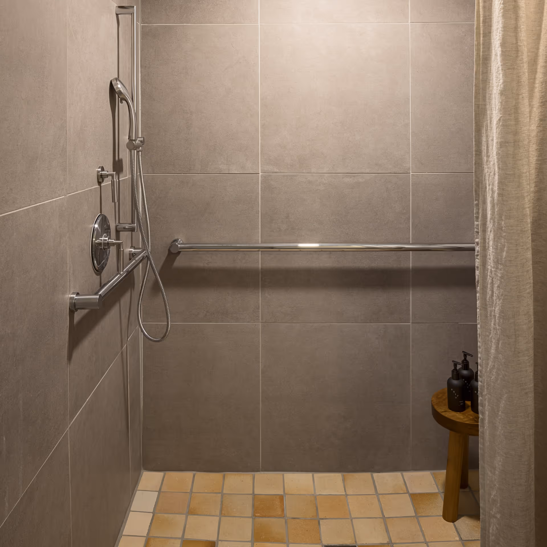 ADA roll-in shower with handheld showerhead, horizontal grab bars, and non-slip tile floor behind a curtain at a boutique hotel bathroom.