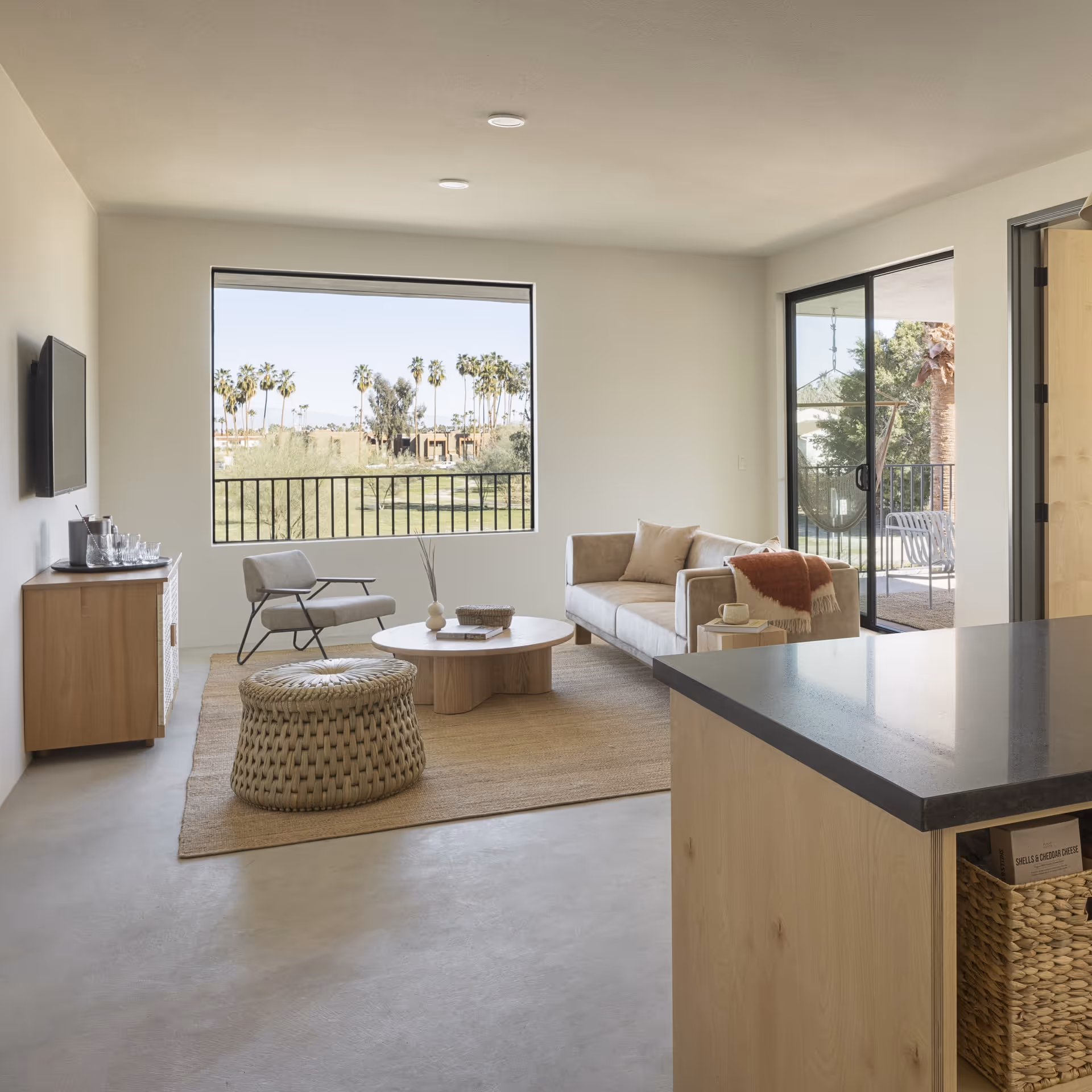 Bright modern living room with minimalist decor, neutral furniture, large windows, and views of palm trees and desert landscape.