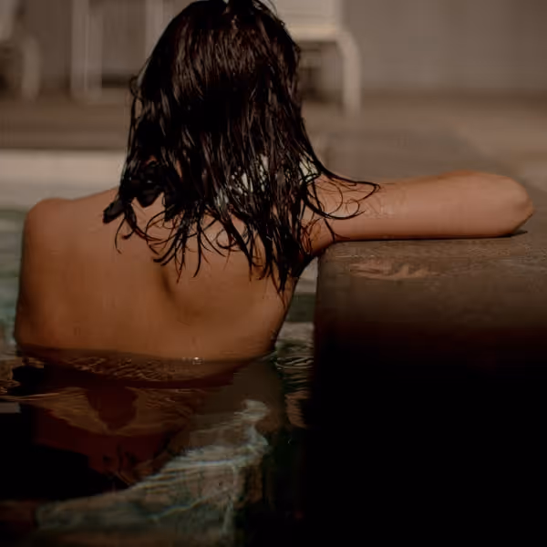 Person relaxing in a warm indoor pool with wet hair, leaning on the pool edge at a modern bathhouse spa.
