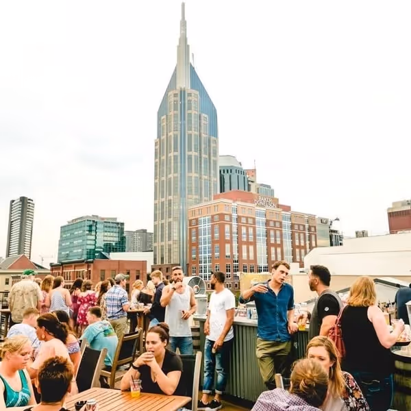 Rooftop bar in downtown Nashville filled with people enjoying drinks and city skyline views with iconic skyscrapers in the background.