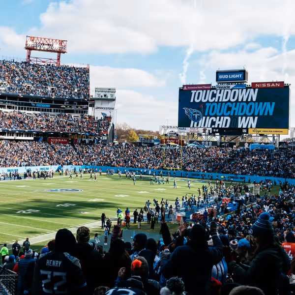 Fans cheering at Nissan Stadium during a Tennessee Titans football game, celebrating a touchdown under a clear blue sky.