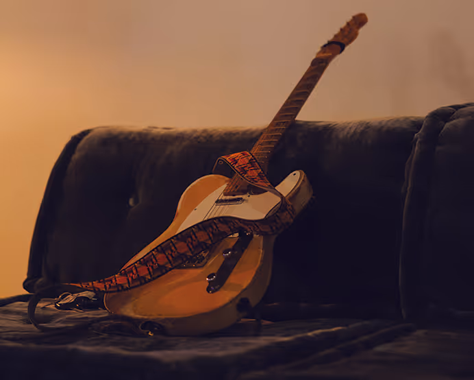 Electric guitar resting on a dark couch, set for a live sound bath or music session in a warm room.
