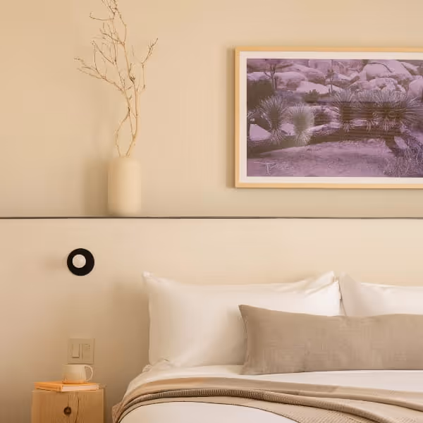 Minimalist hotel bedroom with neutral tones, framed desert artwork, cozy bedding, and modern bedside decor.