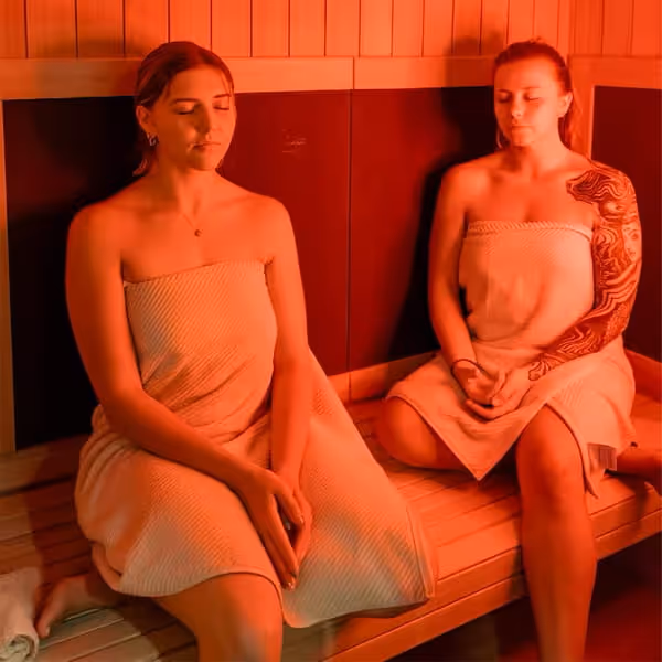 Two women relaxing in a warm sauna, wrapped in towels, enjoying a peaceful wellness and spa experience.