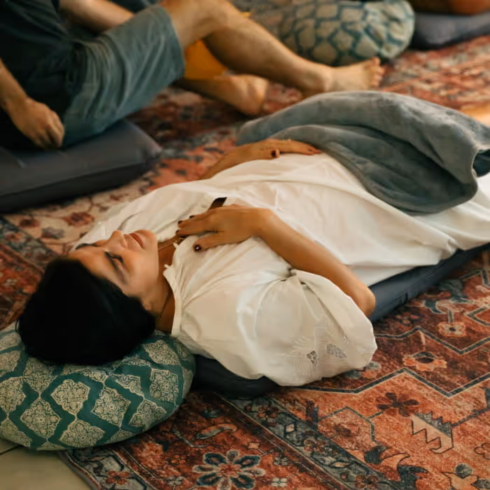 Woman lying on meditation cushion during a guided sound healing session on a Persian rug