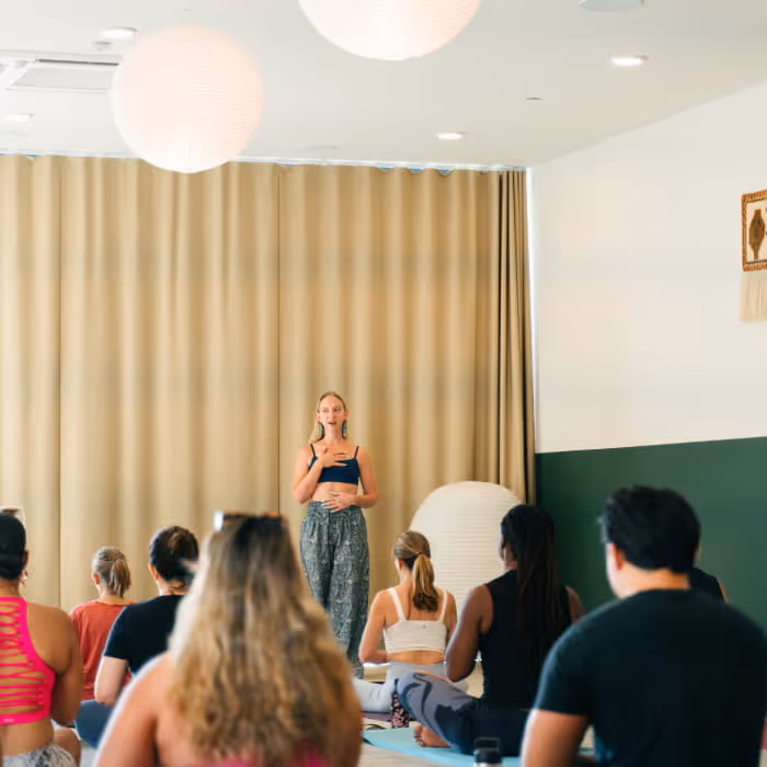 Yoga instructor leading a breathwork session in front of a seated group in a modern studio