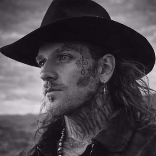 Black and white portrait of tattooed man with face tattoos wearing wide-brim cowboy hat and cross earring