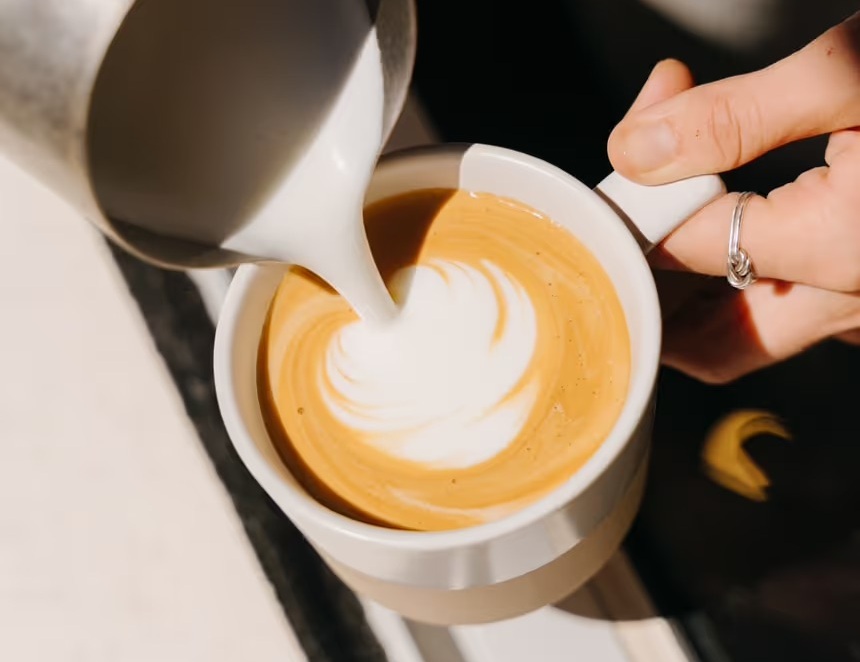 Close-up of barista pouring steamed milk to create latte art in a white cup of specialty coffee at a modern café.