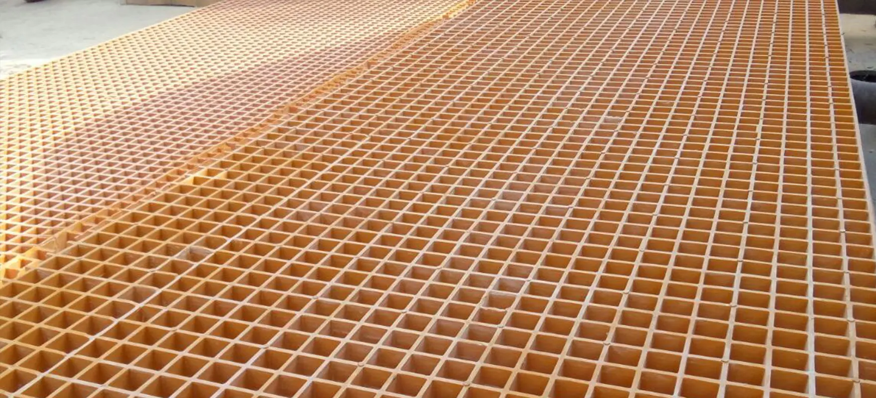 Close-up view of large yellow fiberglass grating panels with square holes stacked side by side.