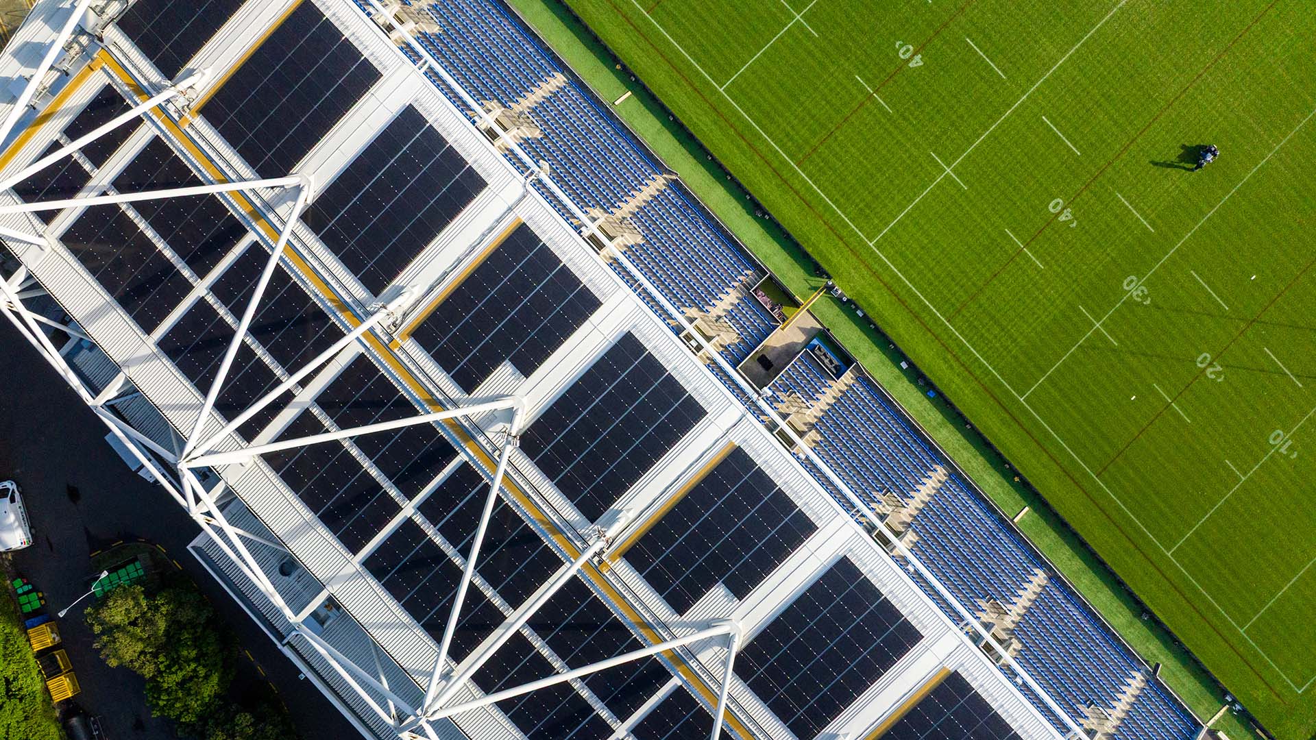 Top-down view of Go Media Stadium’s East Stand, now fully lined with solar panels. The black grid of panels contrasts against the white steel beams and blue seating below, while the lush green pitch fills the right of frame. This image captures sustainability at scale, a stadium transformed into New Zealand’s first solar-powered sporting venue