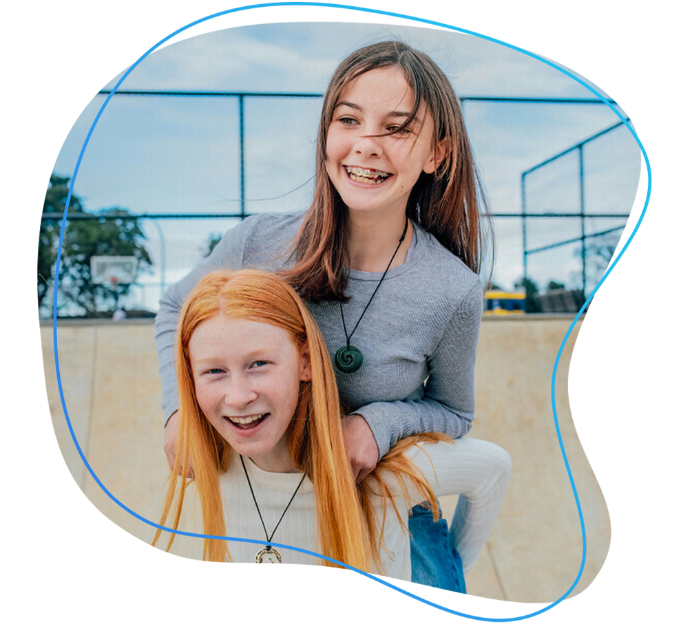Two smiling young girls. One is giving the other a piggy back ride