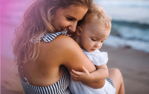 Ung mor med sin baby på stranden en sommerdag