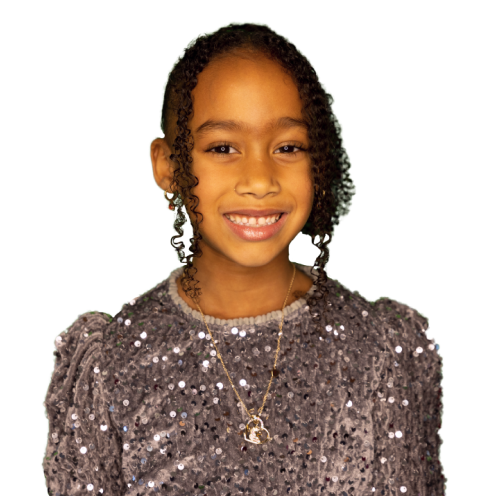 Smiling young girl with curly hair wearing a shiny sequined purple top and a gold necklace.