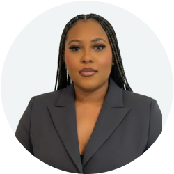 Professional portrait of a woman with long braided hair wearing a dark blazer against a light background.