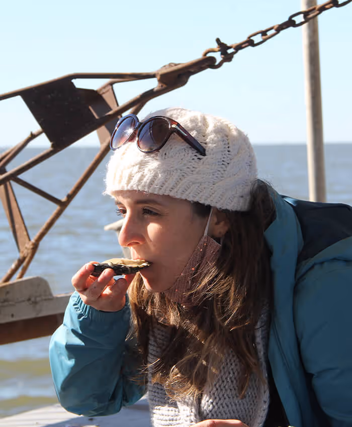 young girl in winter hat eating a raw oyster on a boat in the sun