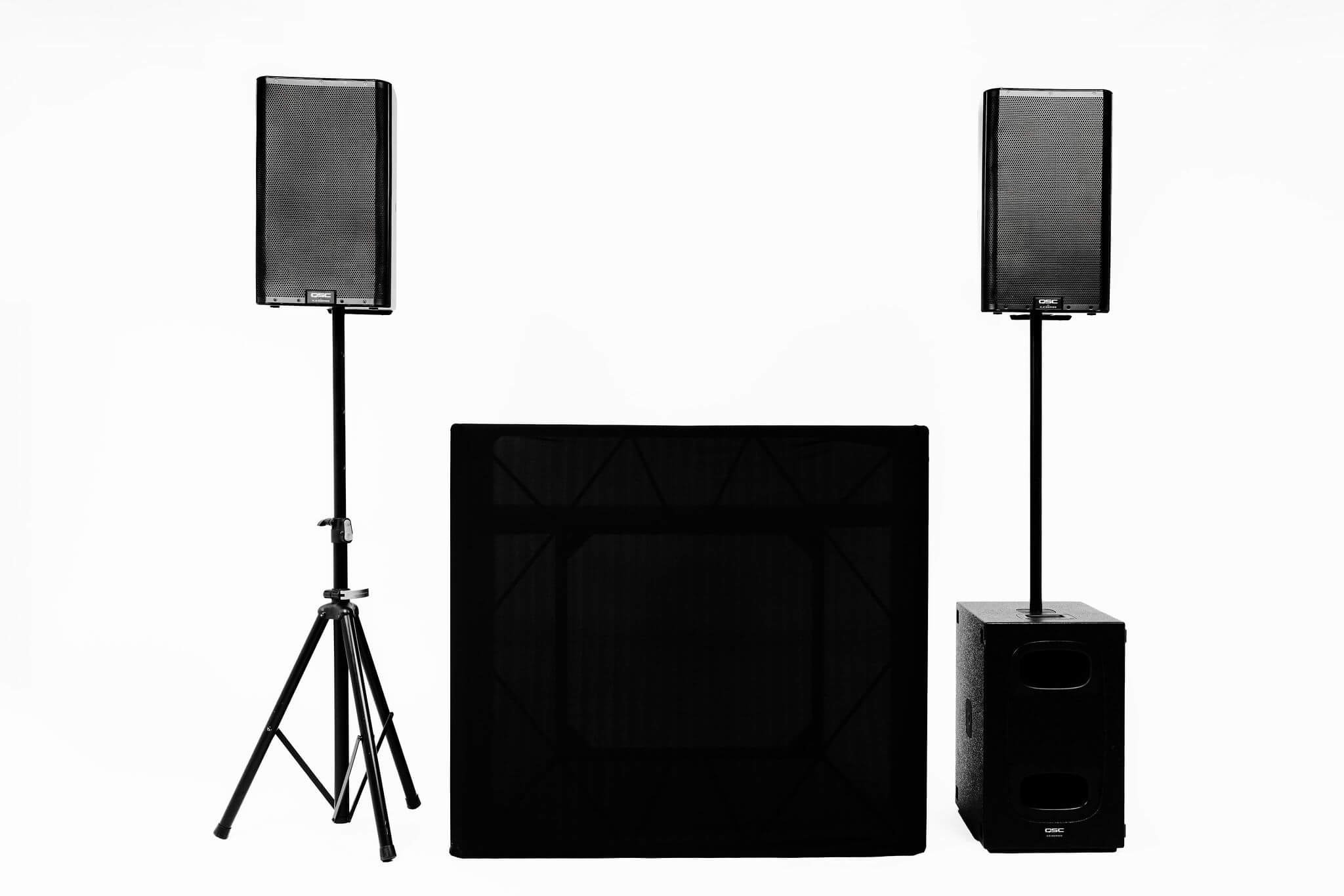 Two black speakers on stands with one subwoofer and a DJ booth with a black cover in the center.