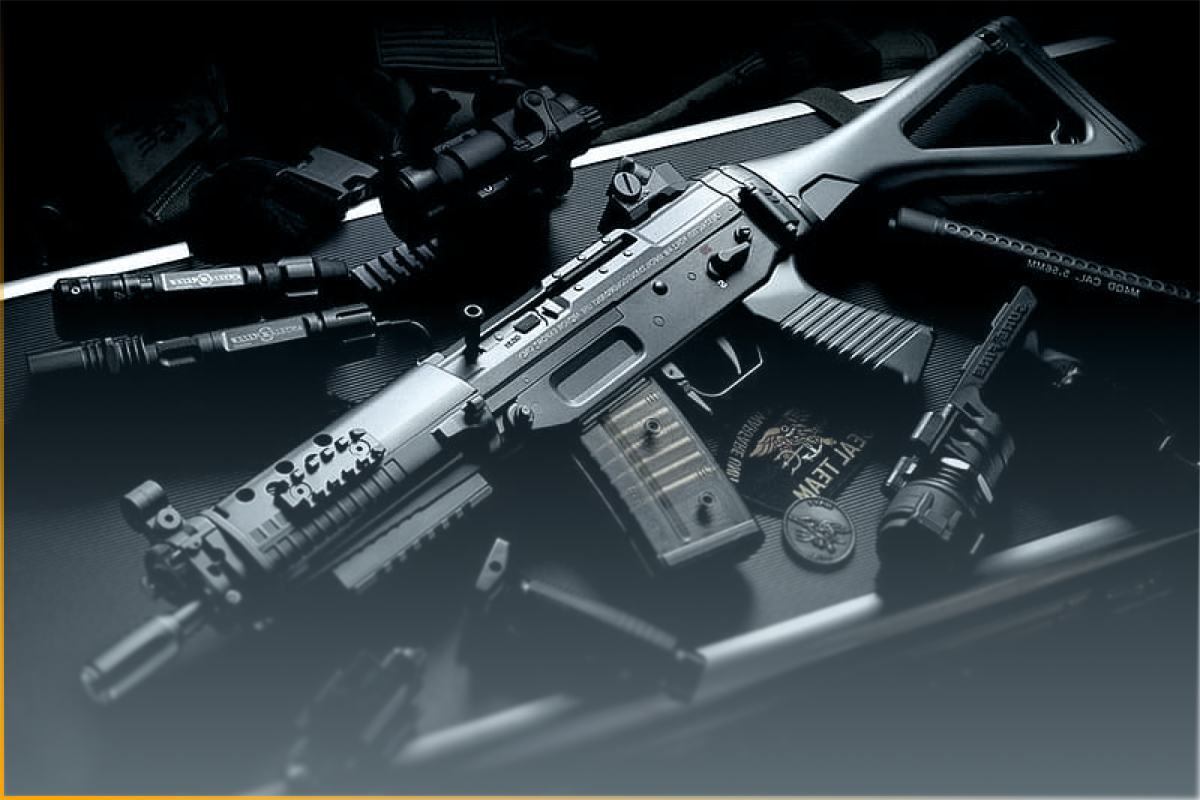 Tactical assault rifle with accessories like scope, flashlight, and magazines on a black case.