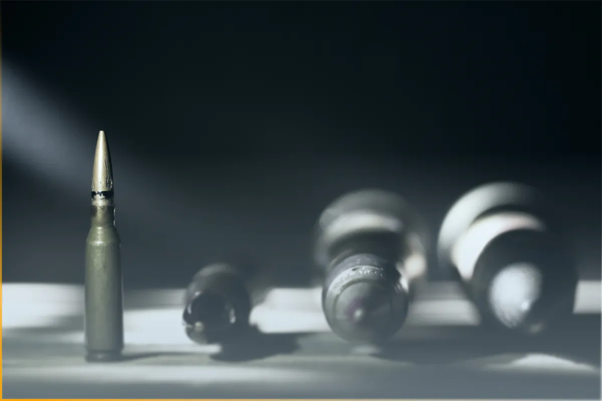 Close-up of a rifle bullet standing upright with other blurred bullets lying behind it on a surface.
