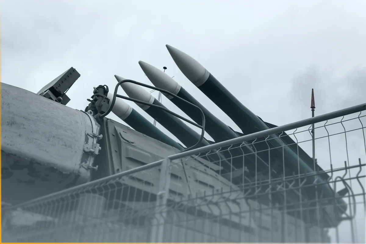 Four large missiles mounted on a military launcher behind a chain-link fence on a cloudy day.