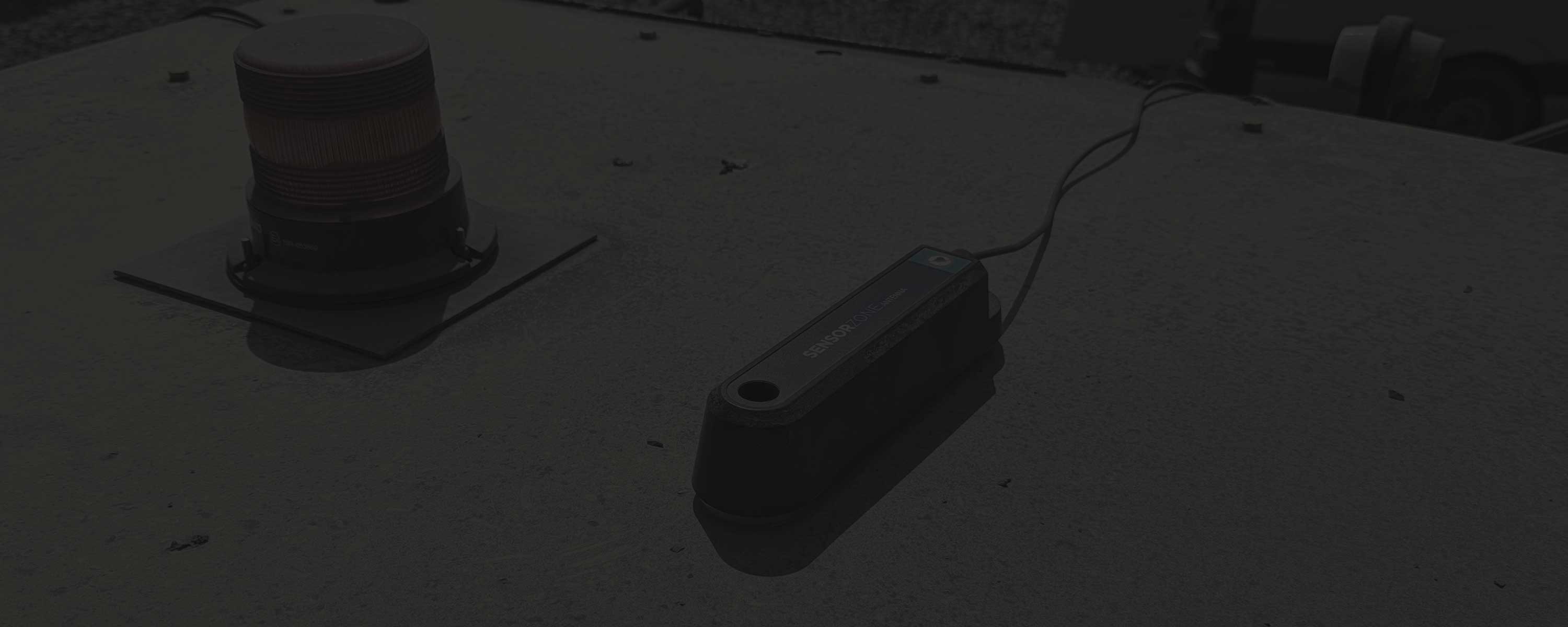 A partially greyed out heading image of a SensorZone alarm beacon and antenna, mounted on top of a wheel loader.