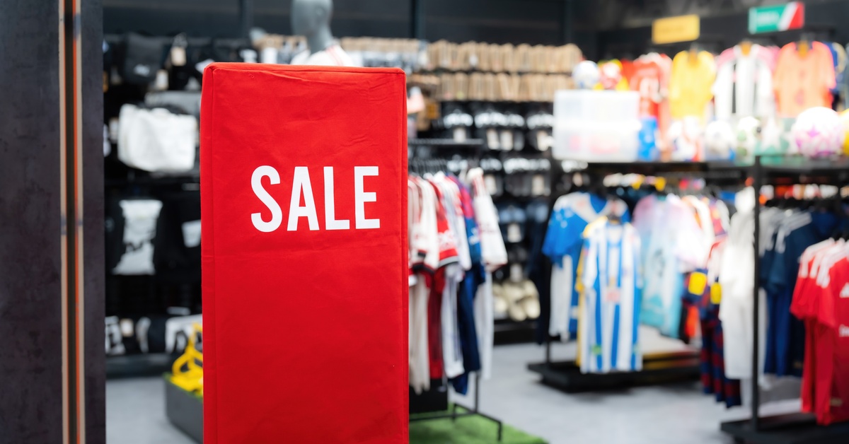 A tall red banner has white text that reads "SALE." A variety of T-shirts are hung up on clothing racks.