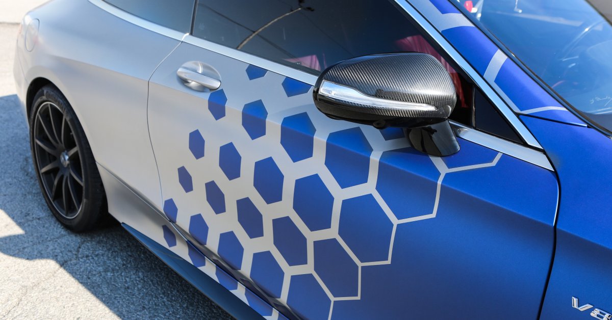 A silver sedan features a vinyl wrap with royal blue hexagons that increase in size until they become a solid color.