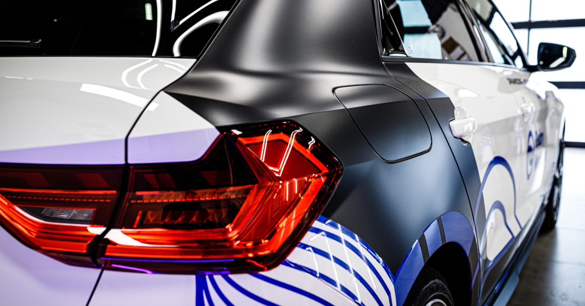 The backside of a car parked in a garage. The vehicle has a white base, black accents, and royal blue stripes.