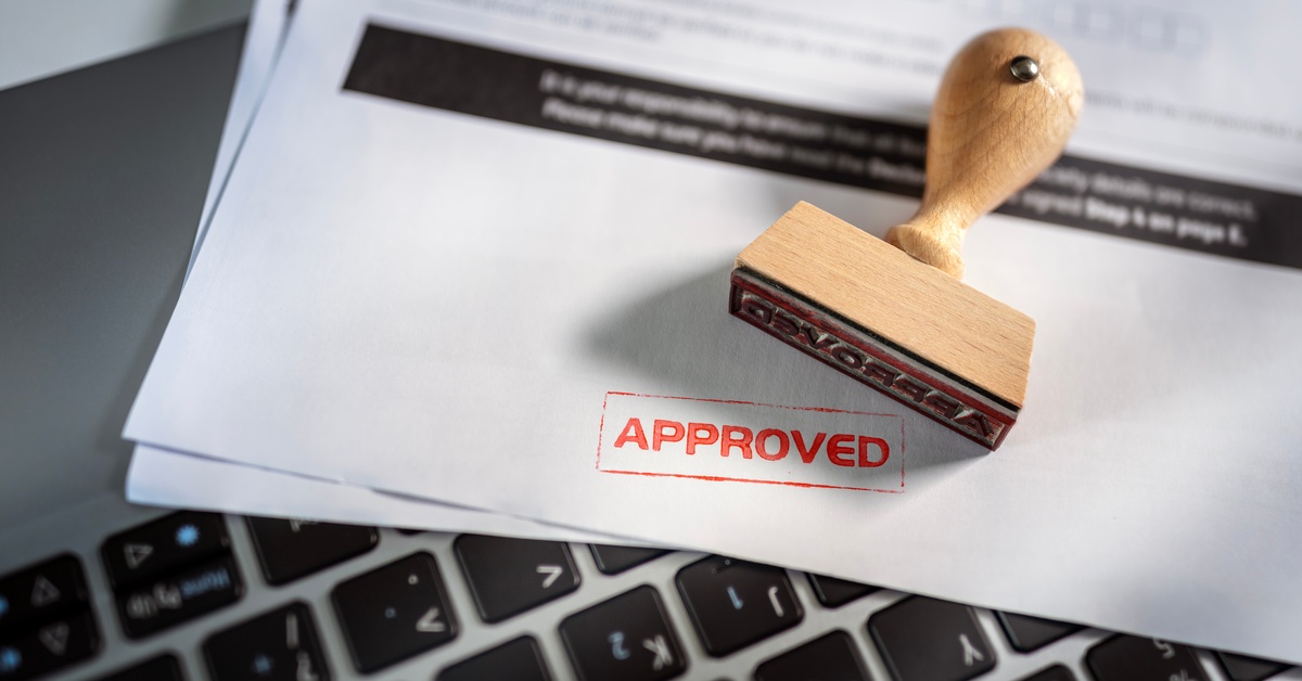 A close-up of a document with a red "APPROVED" stamp in the blank space. The brown stamp lies on the paper.