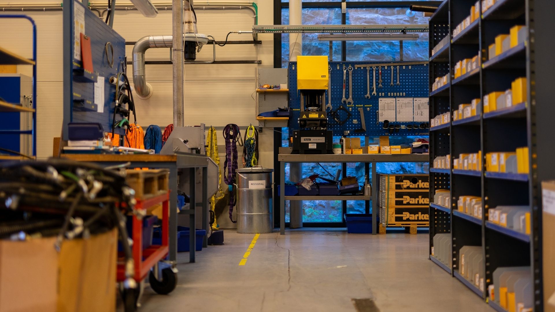 Organized industrial workshop room with tools, hoses, shelves, and equipment under bright lighting.
