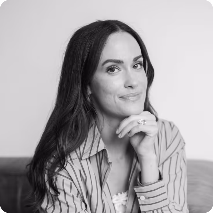 Black and white portrait of Lily Comba with long dark hair resting her chin on her hand.