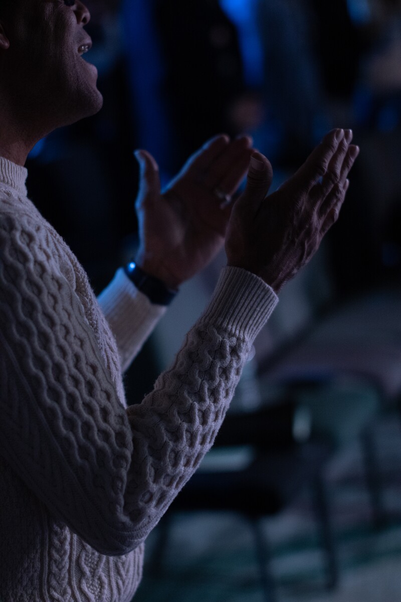 Person wearing a white knitted sweater clapping hands in a dimly lit environment.