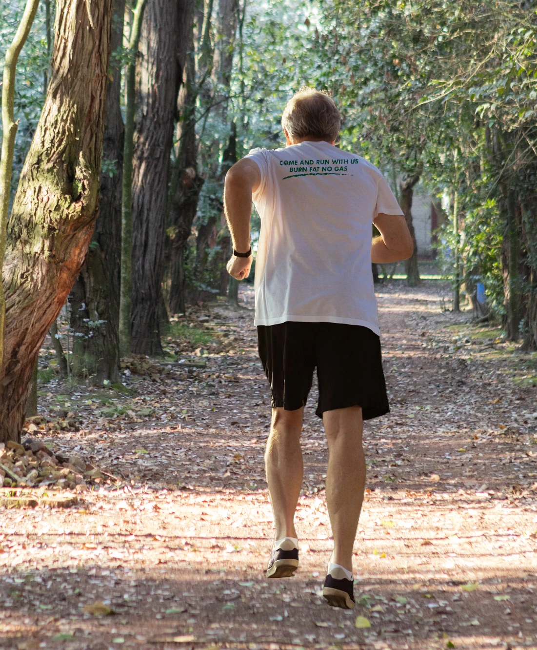 Persona mayor corriendo con camiseta de "The Green Team" y la frase "Come and run with us, burn fat not gas" en la parte trasera.