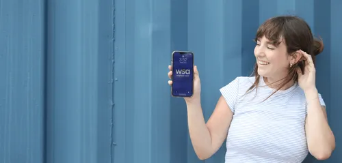 A young woman smiling and holding up her phone showing the WSA logo