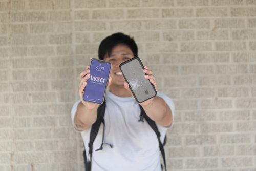 A young man holding up a shattered phone next to a new phone with the WSA logo on the screen