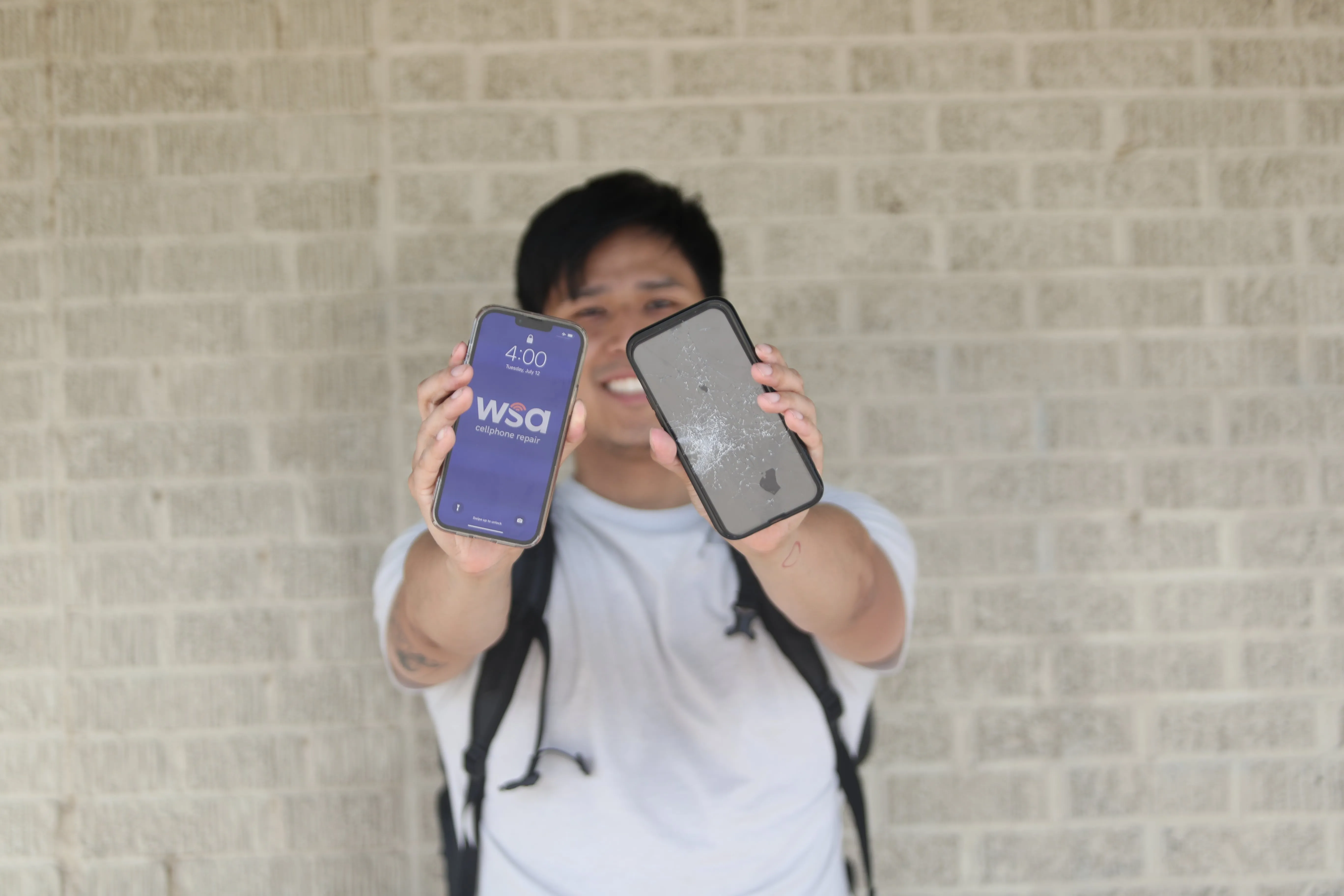 A young man holding up a shattered phone next to a new phone with the WSA logo on the screen